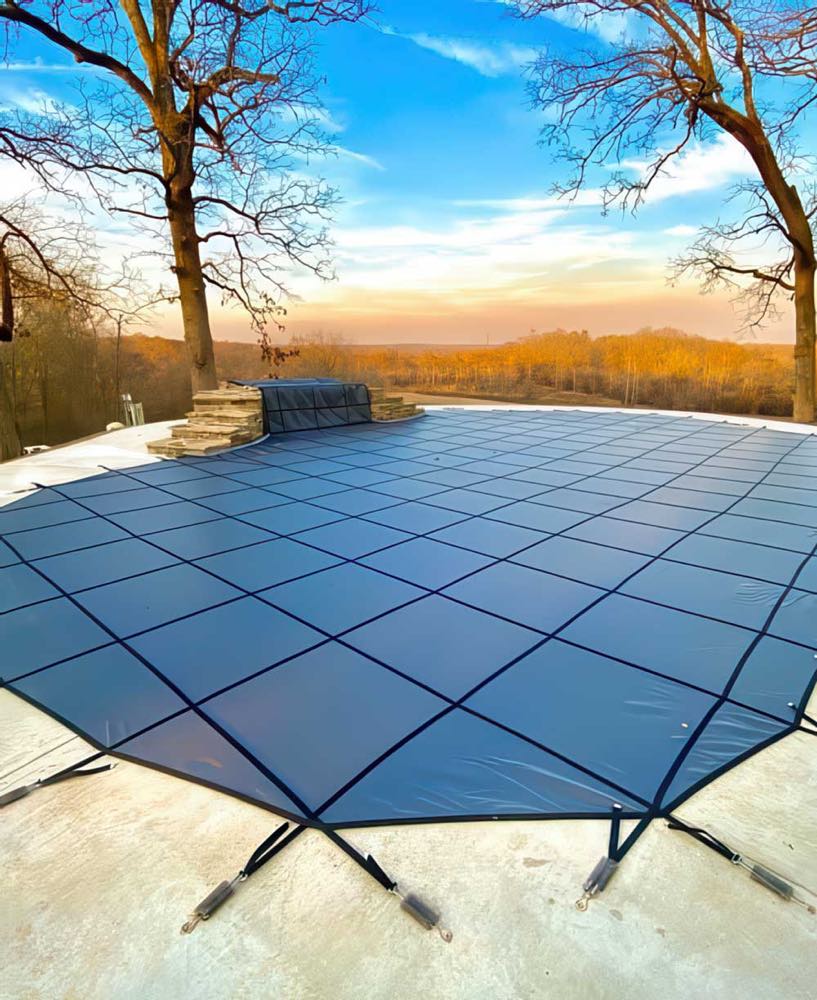 A gray mesh safety cover holding across a pool at sunset